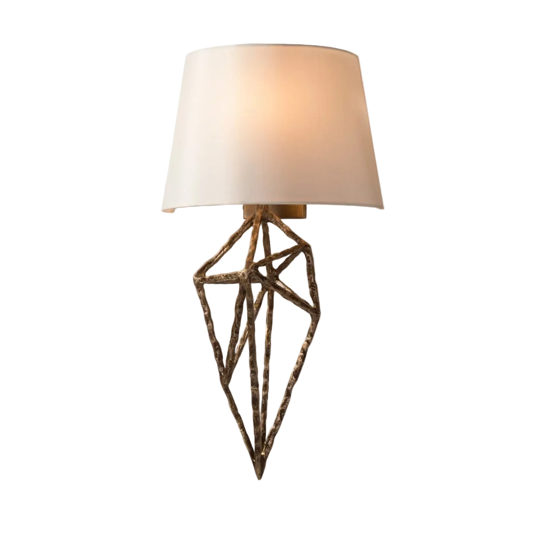 A wall lamp with a geometric brass finish and a white fabric shade.