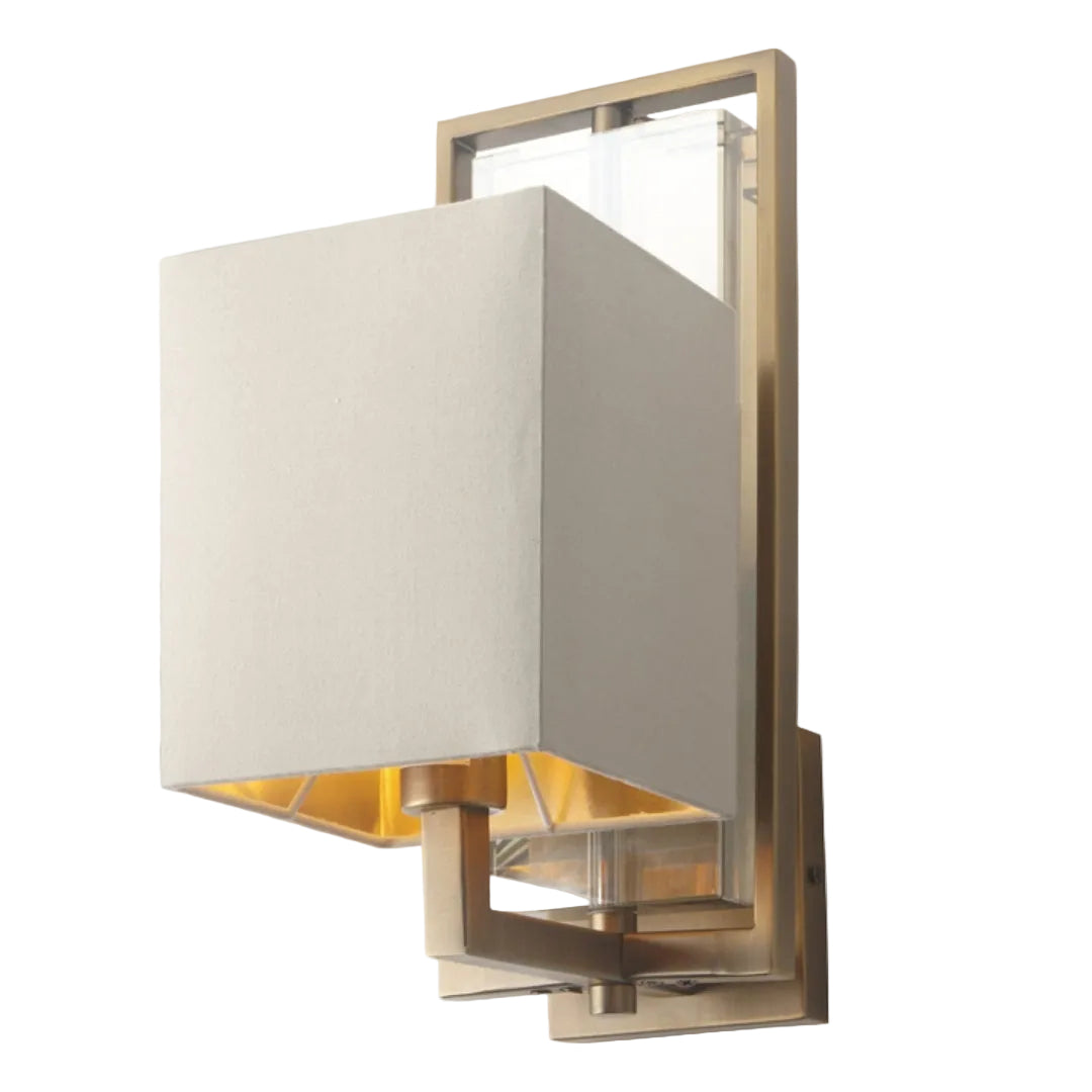 A wall lamp with an antique brass finish featuring a crystal middle and a soft latte fabric shade.