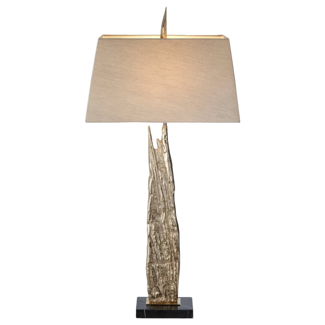 A table lamp with a distressed gold metal base, black marble plinth, and a taupe fabric shade.