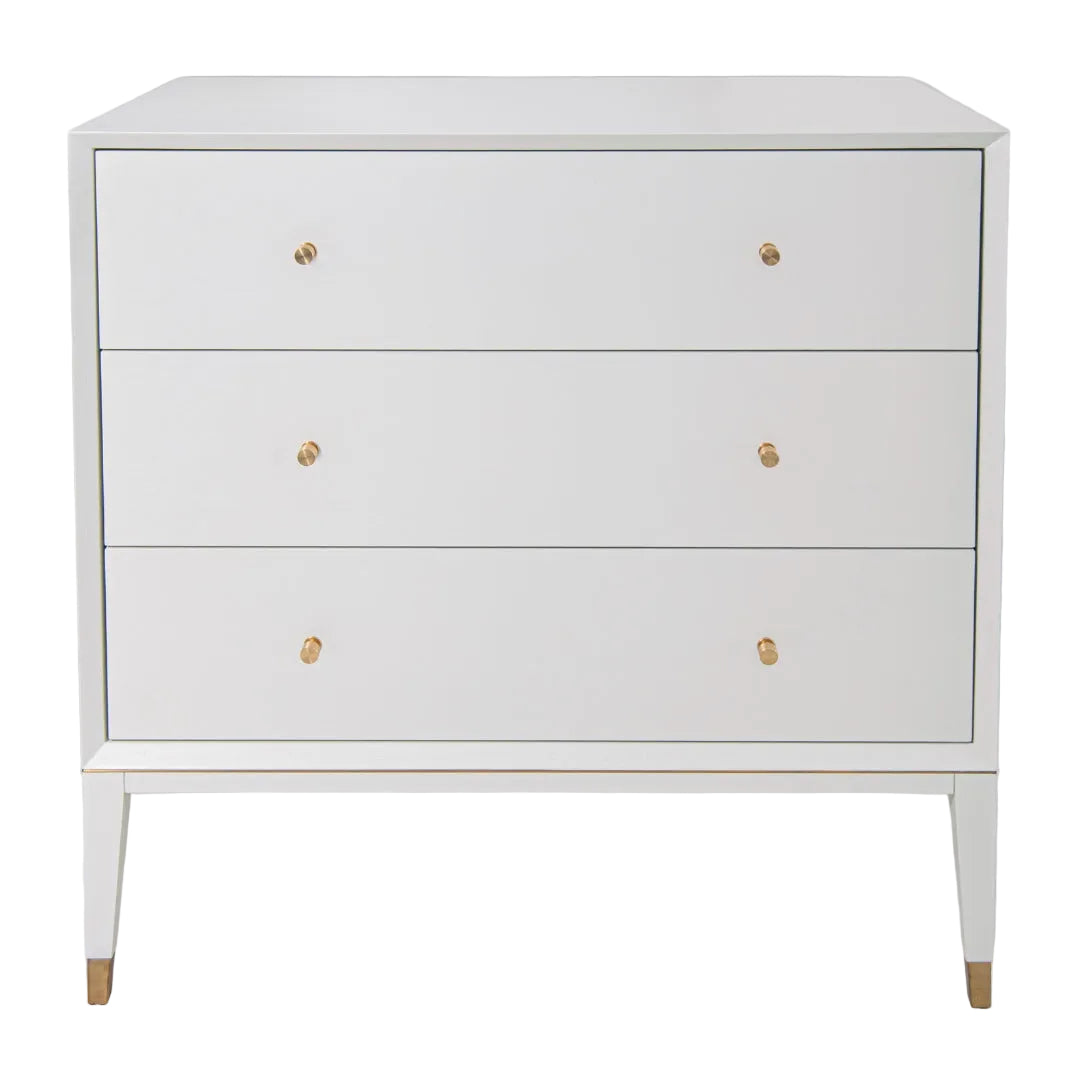 A white Bex 3 Drawer Chest with brushed brass knobs and gold accents on the legs.