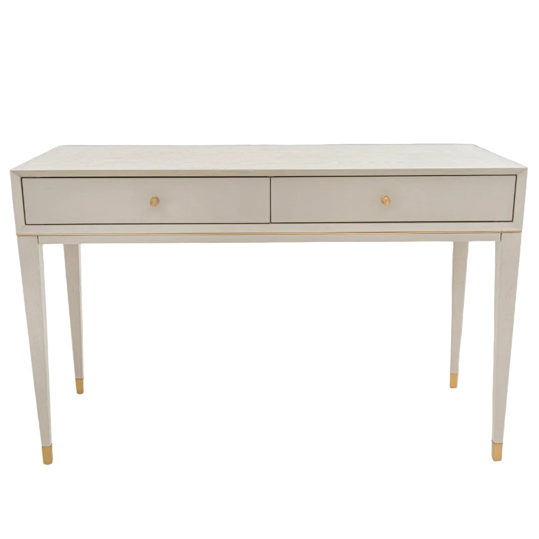 A ceramic grey dressing table with brass trim and gold-colored legs, featuring two drawers.