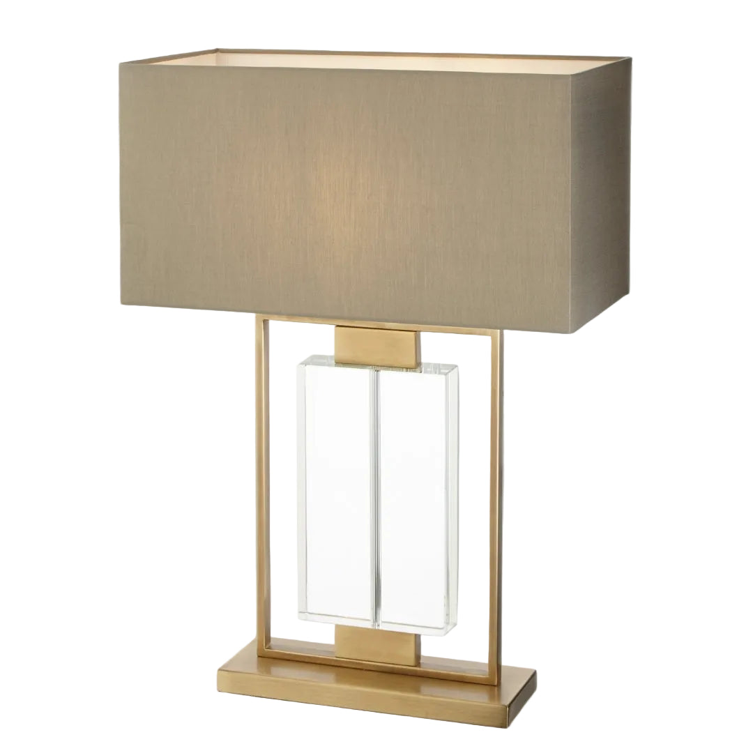 A sculptural table lamp with an antique brass and crystal base, paired with a taupe fabric shade.