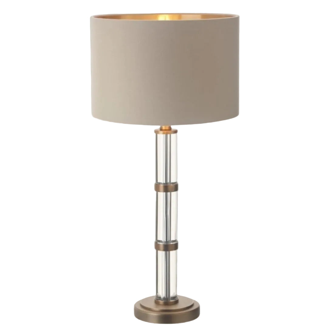 An antique brass finish table lamp with a beige lampshade, featuring crystal accents and a vertical metal structure.
