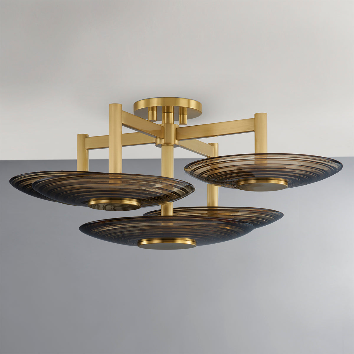 A modern semi-flush mount ceiling light fixture with a brushed gold metal frame and three dark smoked glass shades, shown against a neutral gray and white background.