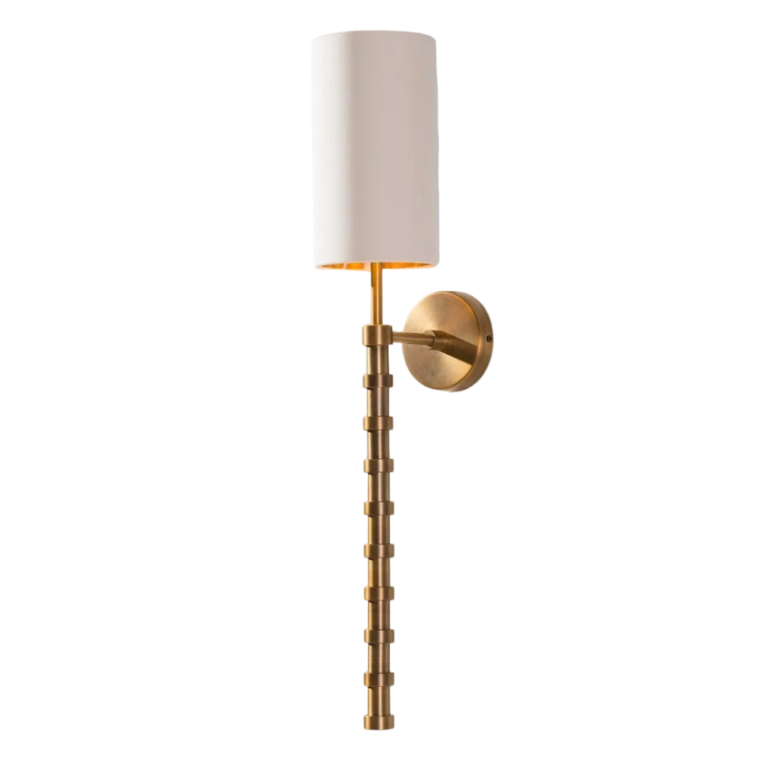 A wall-mounted lamp with an antique brass base and an opal fabric shade, displaying a warm glow.