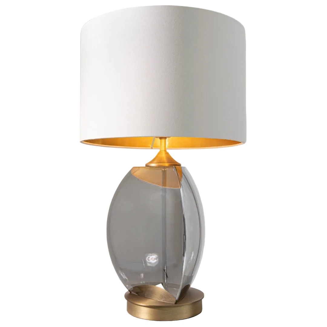 A table lamp with a smoke glass base and antique brass accents, topped with an opal fabric shade lined with gold.