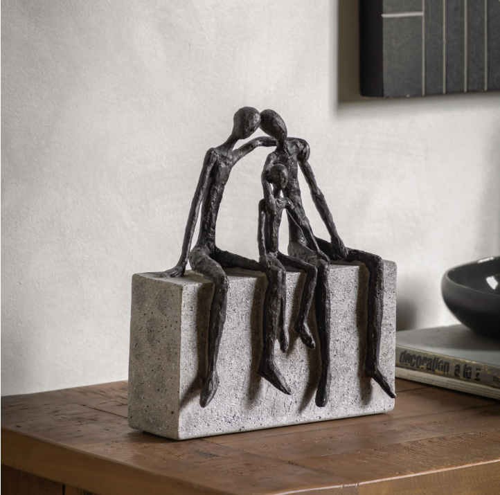 Abstract sculpture of two figures on a rectangular base on a wooden surface.
