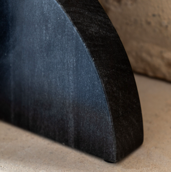 Close-up of a dark charcoal gray stone fireplace hearth piece, showing its textured surface and curved profile against a neutral stone background.