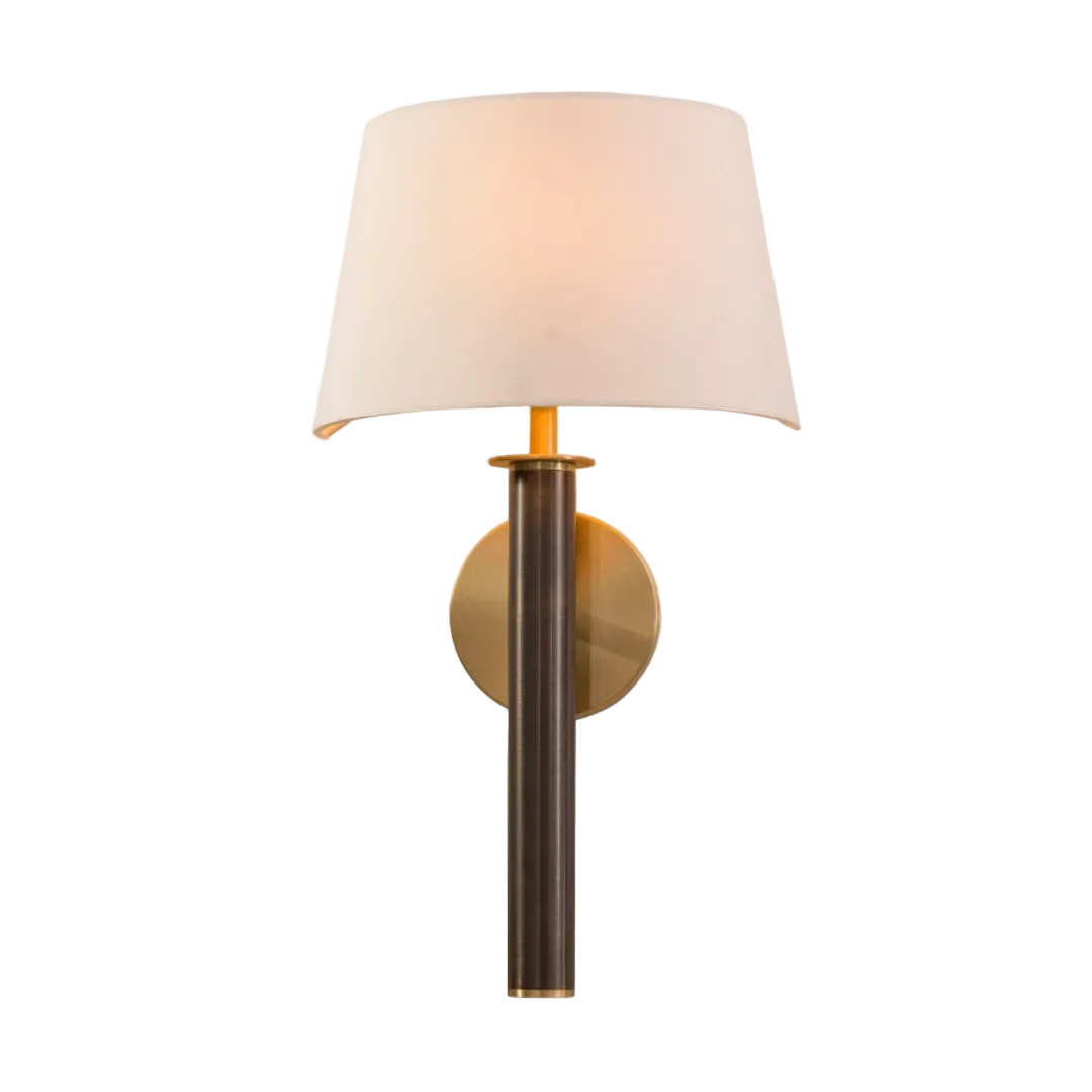 A wall lamp with a dark antique brass tube and base, paired with a light antique brass circular wall mount and an off-white fabric shade.