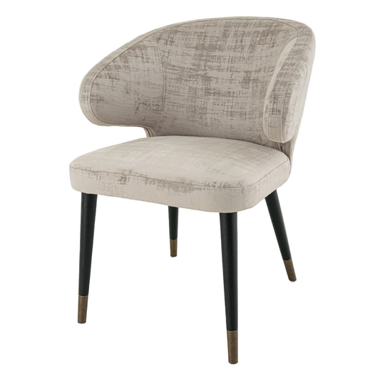 A luxurious upholstered chair with soft mushroom velvet fabric, having a painted black frame with antique brass accents, and dark wood legs with brass-capped feet.