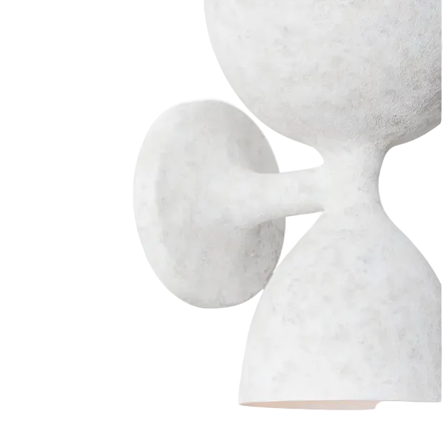 A close-up of a sculptural wall sconce with a textured, stone-like finish in off-white and light gray, featuring a round wall plate and a flared dome shade.