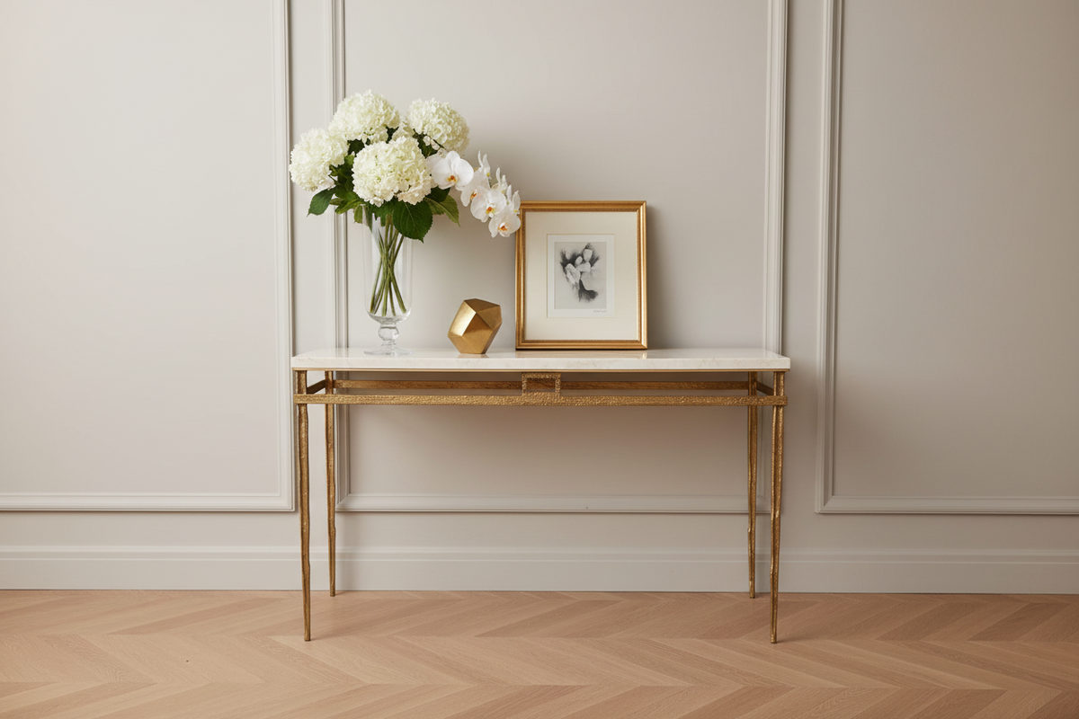 A console table with a light beige marble top and a distressed gold metal frame with slender legs, shown against a plain white background.